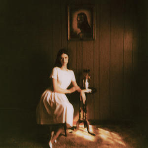 Ethel Cain - Preacher's Daughter Cover art of Ethel Cain's Preacher's Daughter.
It depicts Ethel sitting on a chair wearing a white dress.
Her arm is resting on a side table.
Above her on the wall hangs a portrailt of a man with a beard and long hair.